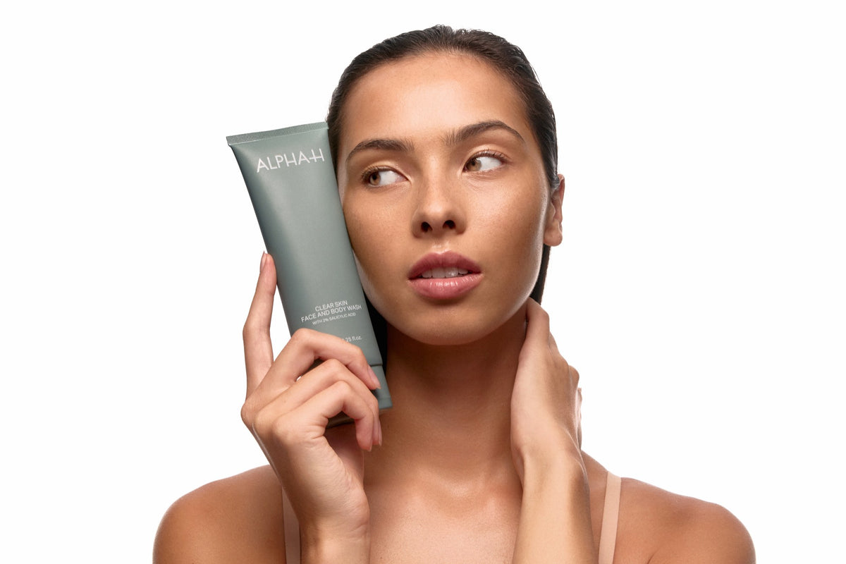 Alpha-H Clear Skin Face & Body Wash modelo con el tubo junto al rostro