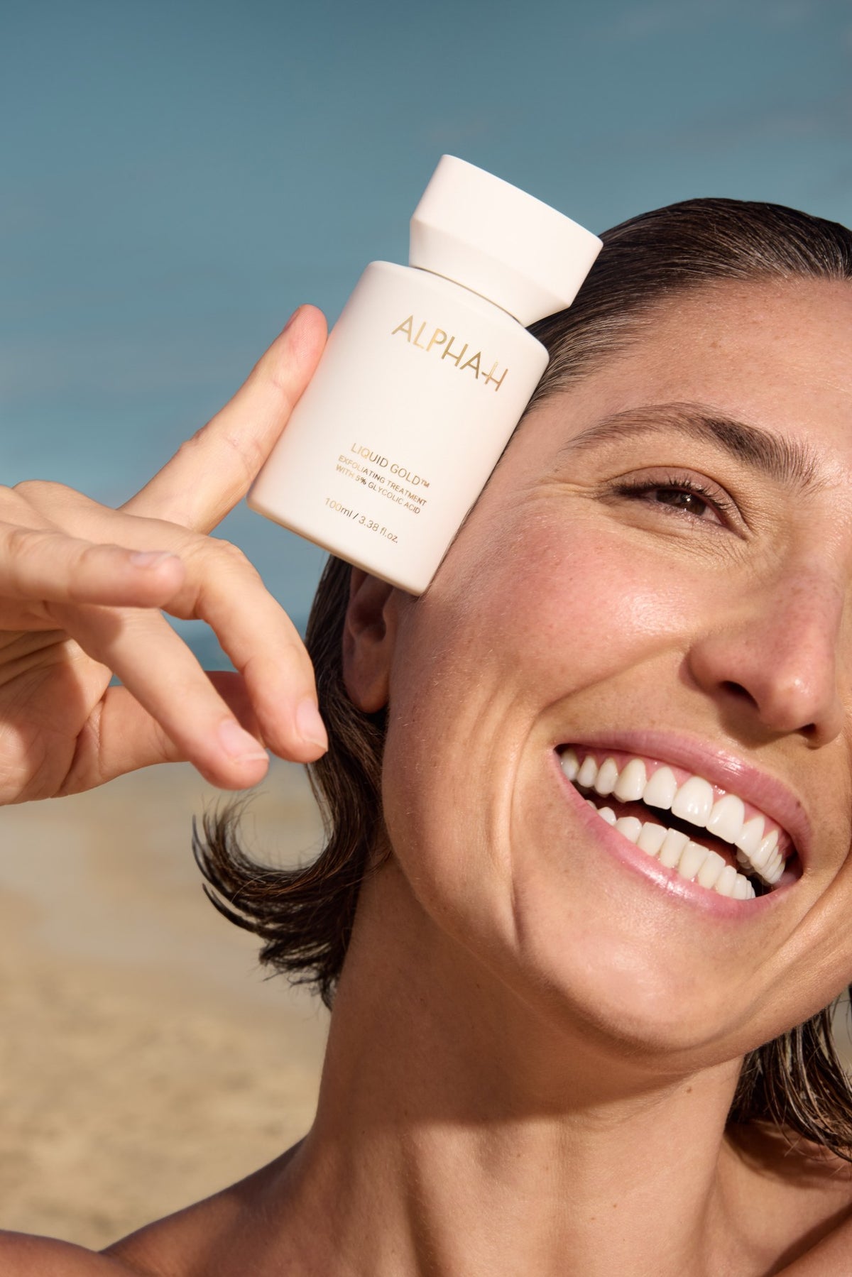 Alpha-H Liquid Gold Exfoliating Treatment modelo con el frasco junto al mar