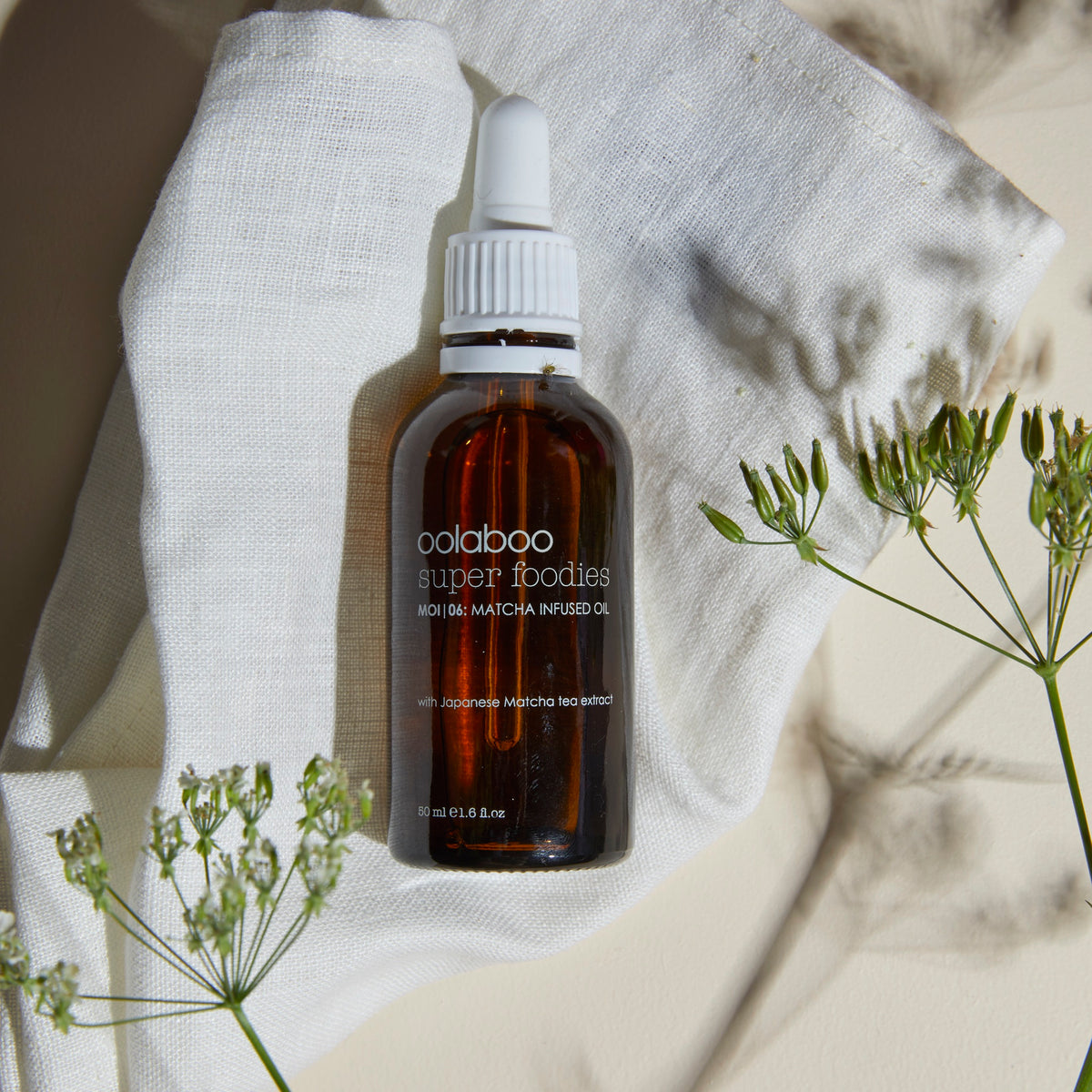 Oolaboo Super Foodies Matcha Infused Oil sobre paño de lino con flores